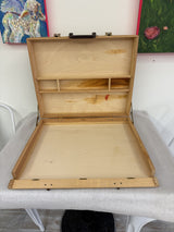 Open wooden artist supply case showing storage compartments and paint marks